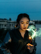 © Jesse Morrow/Stocksy - Young woman with sparkler firework in hand on rooftop at dusk
