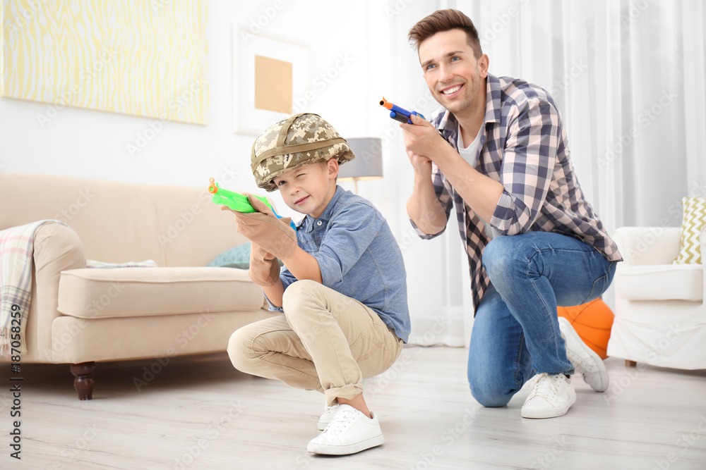 Cute boy and his father playing with toy guns at home