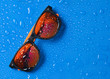 Fashion sunglasses in drops of water on a bright blue background. Top view.