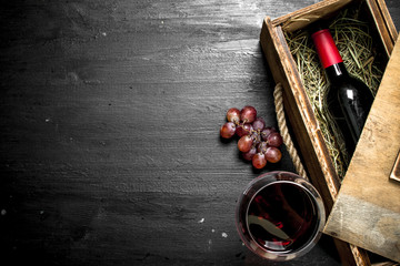 bottle of red wine in an old box with a branch of grapes.