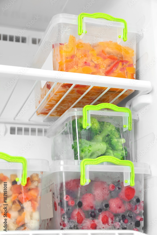 Containers with frozen berries and vegetables in freezer, closeup