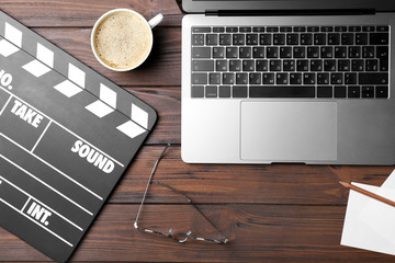 Movie clapper and laptop on wooden background, top view