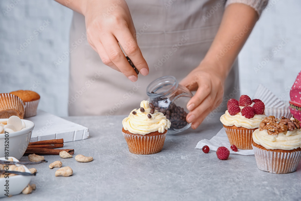 Female baker decorating tasty cupcake with chocolate at table