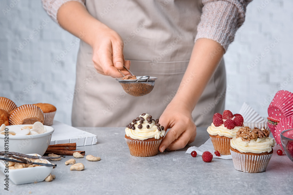 Female baker decorating tasty cupcake with cinnamon at table
