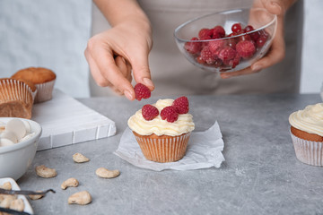 Sticker - Female baker decorating tasty cupcake with raspberries at table