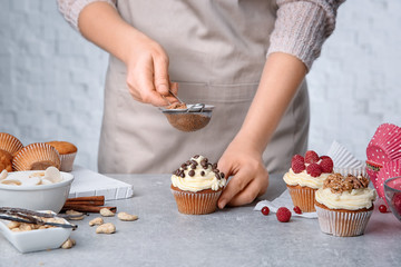 Sticker - Female baker decorating tasty cupcake with cinnamon at table