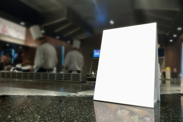 Mock up Menu frame on Table in Bar restaurant ,Stand for booklets with white sheets of paper acrylic tent card on cafeteria blurred ,Chef cooking in background.