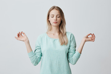 Wall Mural - Restful peaceful blonde female feels relaxed, stands in lotus pose, tries to concentrate or to be focused, closes eyes, enjoys silence, tries to find balance. Calm atmosphere and meditation