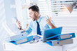 © zinkevych - Irritated. Emotional young irritated worker sitting at the table covered with folders and looking at the smartphone in his hands while shouting