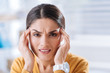 © zinkevych - Terrible migraine. Tired young frowning woman touching her forehead and feeling awful while having a terrible migraine when being at work