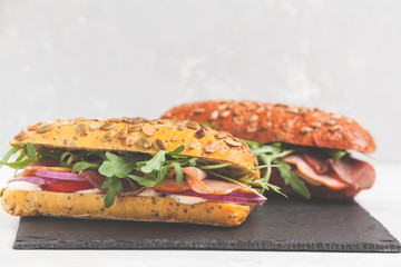 Canvas Print - Sandwiches with ciabatta, meat, bacon, vegetables and cream sauce on black slate. Fast food concept.