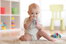 Pretty Baby Boy Drinking Water From Bottle. Kid Sitting On Carpet In Nursery At Home. Smiling Child Is 7 Months Old.