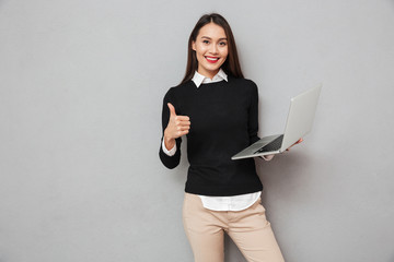 Wall Mural - Pleased asian woman in business clothes holding laptop computer