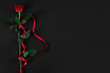 One dark red rose with red ribbon on black background. Romantic 
