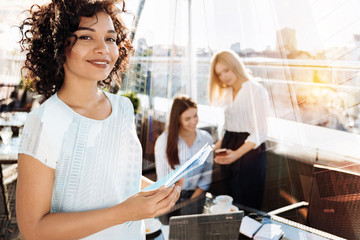 Wall Mural - My friends. Delighted brunette keeping smile on her face and holding documents while standing on the foreground