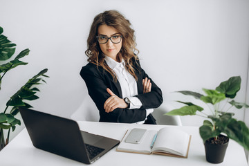 Attractive business woman sits at the desk at her workplace, with laptop, mobile phone, and notebook