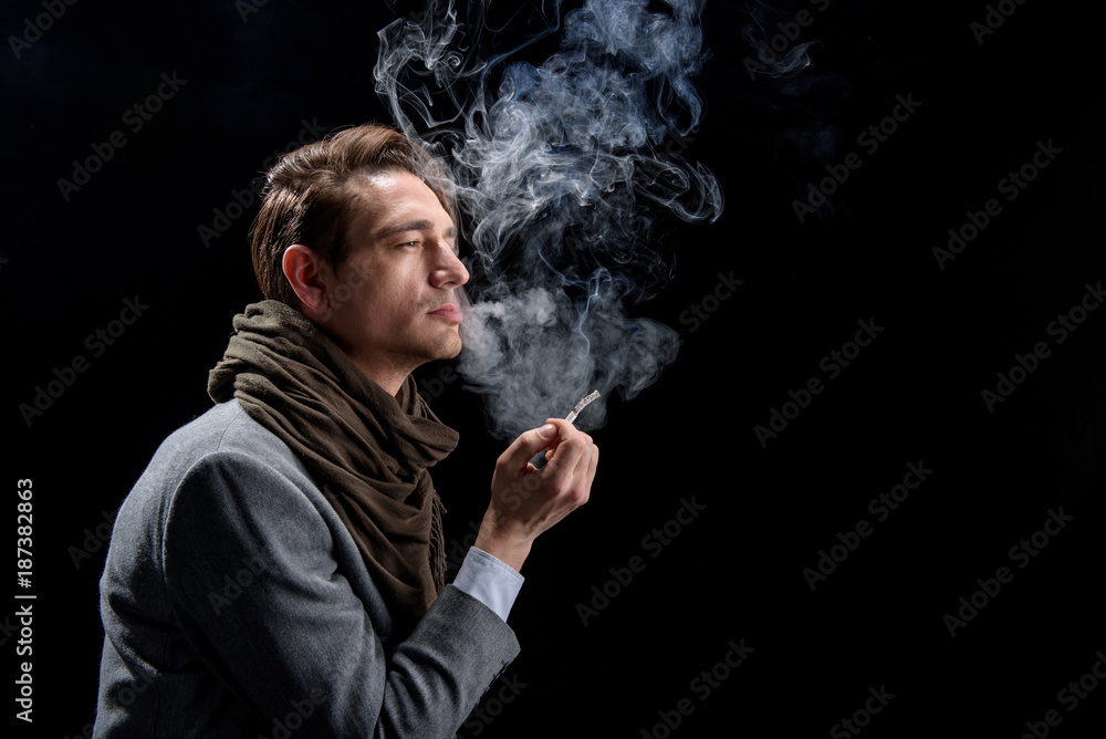 Depression. Side view profile of sad young stylish man is standing and  enjoying cigarette. He is