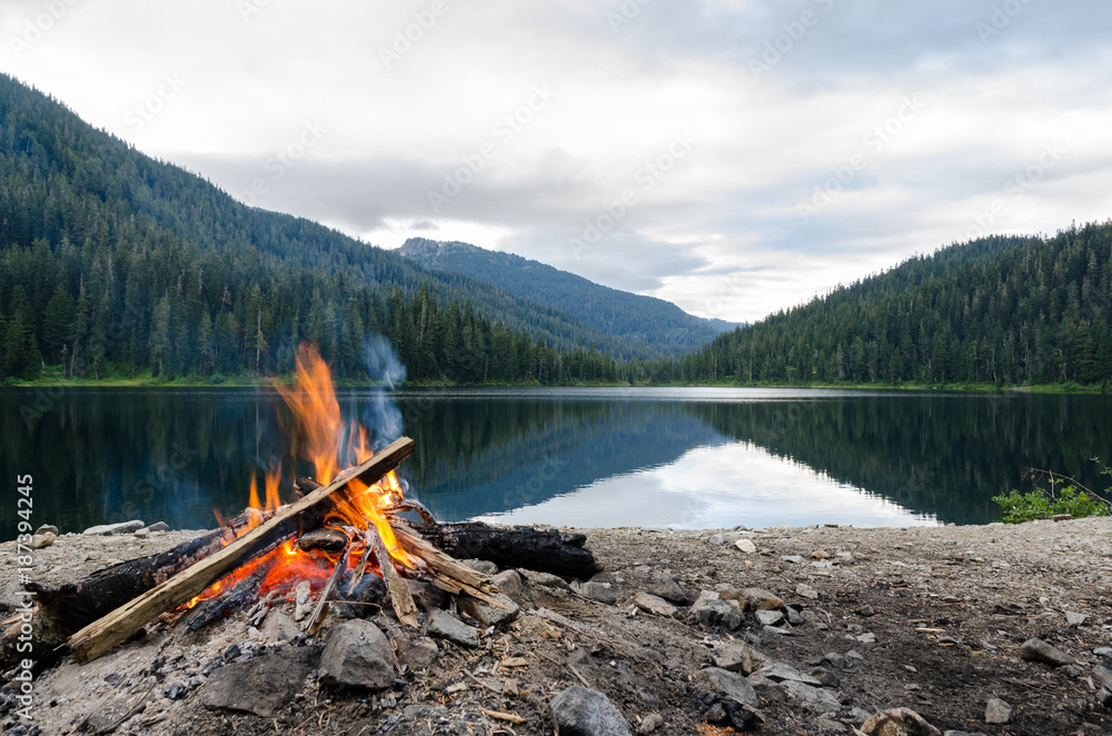 Landscape of a campfire in a peaceful lake valley. - obrazy, fototapety, plakaty 