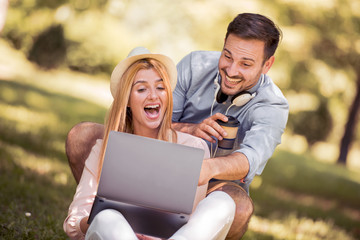 Wall Mural - Young couple sitting on the grass and using laptop.