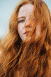 © Smith & Turner Creative Services/Stocksy - Close up portrait of a young woman with ginger hair and freckles with her hair blowing over her face on a wintery day