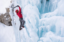 Young Woman Wearing Red Jacket Ice Climbing On Frozen Waterfall