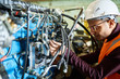 © Seventyfour - Profile view of concentrated young technician wearing protective helmet repairing hydraulic excavator system while standing at spacious heavy equipment factory