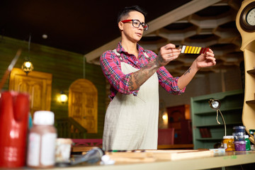 Canvas Print - Portrait of tattooed female artist wearing apron looking at color swatches choosing color palette for design project in modern workshop