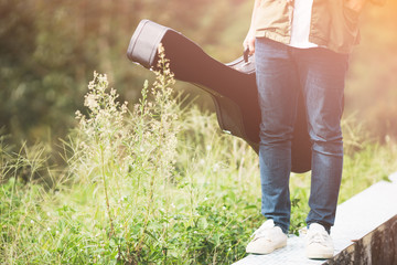 Man dressed in jeans holding guitar case in nature outdoo