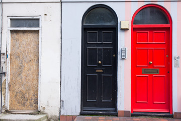 Wall Mural - Black door next to a red door and a wooden panel replacing a missing door in the front facade of a Victorian British English house