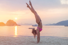 Young Fitness Woman Doing Handstand Exercise On Beach At Sunrise. Sporty Girl In Bikini Practicing Yoga Seashore.
