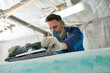 Portrait of worker wearing respirator repairing boat in yacht workshop using electric polishing tool, focus on foreground