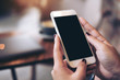 © Farknot Architect - Mockup image of woman's hands holding mobile phone with blank black desktop screen in cafe