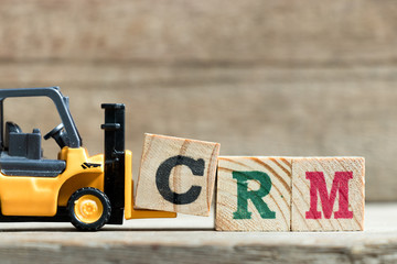 Wall Mural - Toy yellow forklift hold letter block  to complete word CRM (Abbreviation of Customer Relationship Management)on wood background