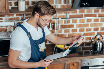 handsome young foreman in protective workwear writing on clipboard