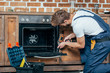 © LIGHTFIELD STUDIOS - young repairman in protective workwear fixing oven with electric drill