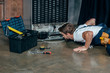 © LIGHTFIELD STUDIOS - young handyman in protective workwear with toolbox looking at broken refrigerator