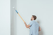 © LIGHTFIELD STUDIOS - side view of smiling young man using paint roller while painting wall at home