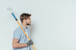 © LIGHTFIELD STUDIOS - side view of young man holding paint roller and looking away on grey