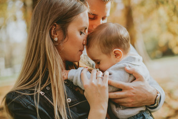 Happy young parents with baby boy in autumn park