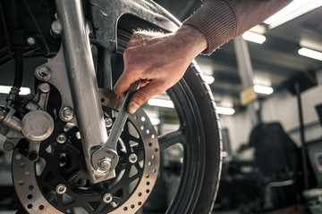 Wall Mural - Close up of man's hand holding mounting wrench near the motorcycle's vehicle. Garage on a background