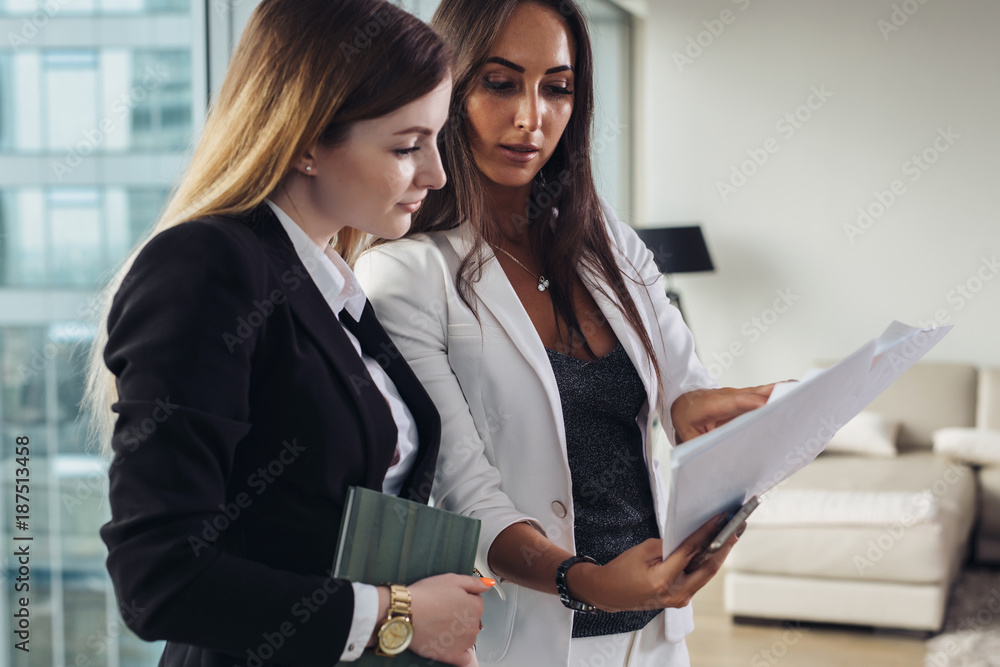 Woman and her assistant holding documents discussing business plan and strategy at workplace - obrazy, fototapety, plakaty 