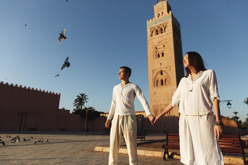 Wall Mural - Dreamy couple dressed in white closes walks around African city Marrakesh in a sunny evening