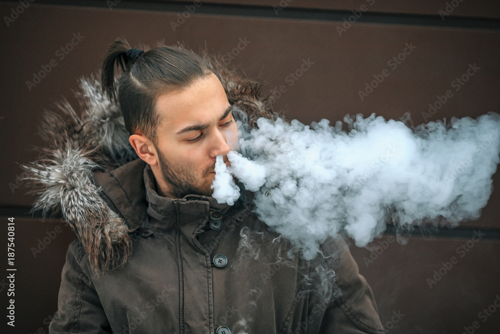 vape man Vape man. Portrait of a handsome young white guy with modern haircut vaping  an electronic cigarette opposite the futuristic urban background.  Lifestyle. Stock-bilde