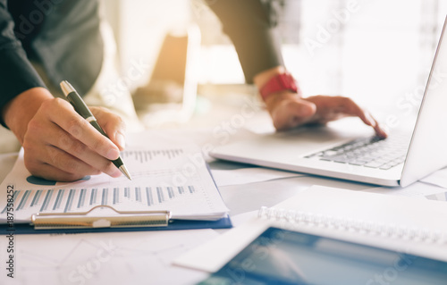 Cuadros en Lienzo Businessman holding pen and pointing paper chart summary analyzing annual business report with using laptop at room office desk