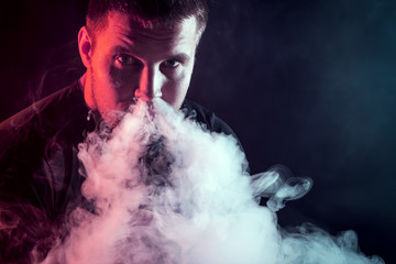 The man smoke an electronic cigarette on the dark background