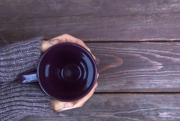 Girl  hands hold an empty in warm woolen knitted sweater cup for coffee / tea, the top view, on the background of a brown wooden table