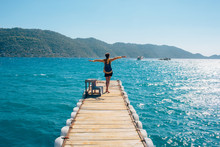 Tourist, Happy Girl With Backpack Standing On A Sea Pier Breathing Fresh Air Raising Hands Enjoying The View. Pier, The Turkish City Of Simena