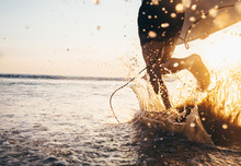 Man Surfer Run In Ocean With Surfboard. Closeup Image Water Splashes And Legs, Sunset Light
