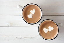 Two Cups Of Hot Chocolate With Heart Shaped Marshmallows Over A White Wood Background