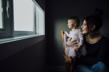 Mother And Daughter Looking Through Window While Sitting On Chair At Home